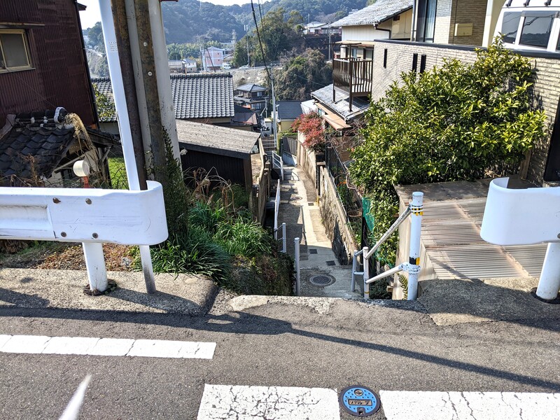 敷地北、東西に延びる市道を東から。階段で下る、細い路地です。